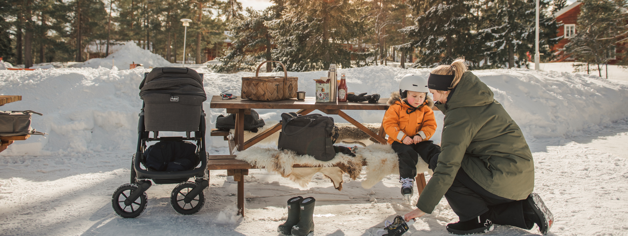 Vuxna och barn med slalomutrustning sitter på liggunderlag i snön.