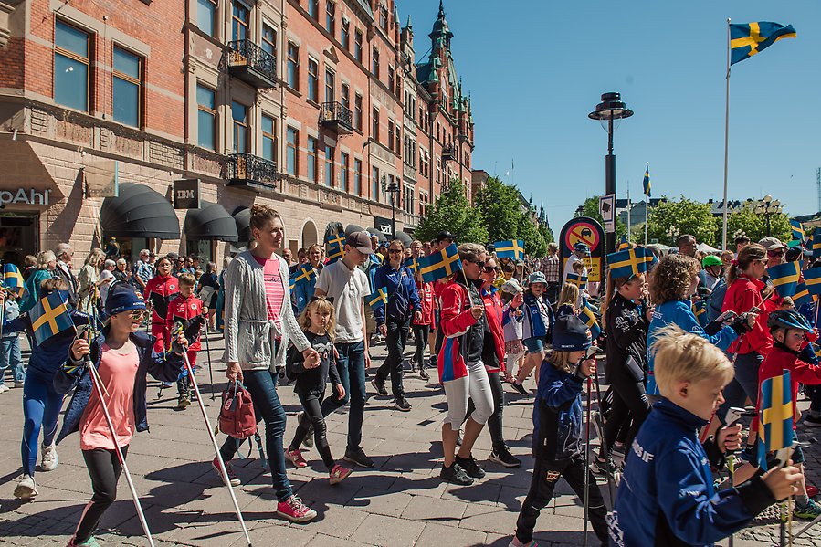 Personer, barn och vuxna, går i flaggparaden. I handen håller dem den svenska flaggan.