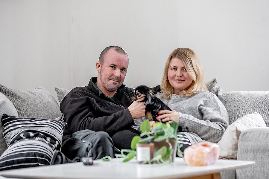 En kvinna och en man sitter i en soffa med sin hund i famnen.