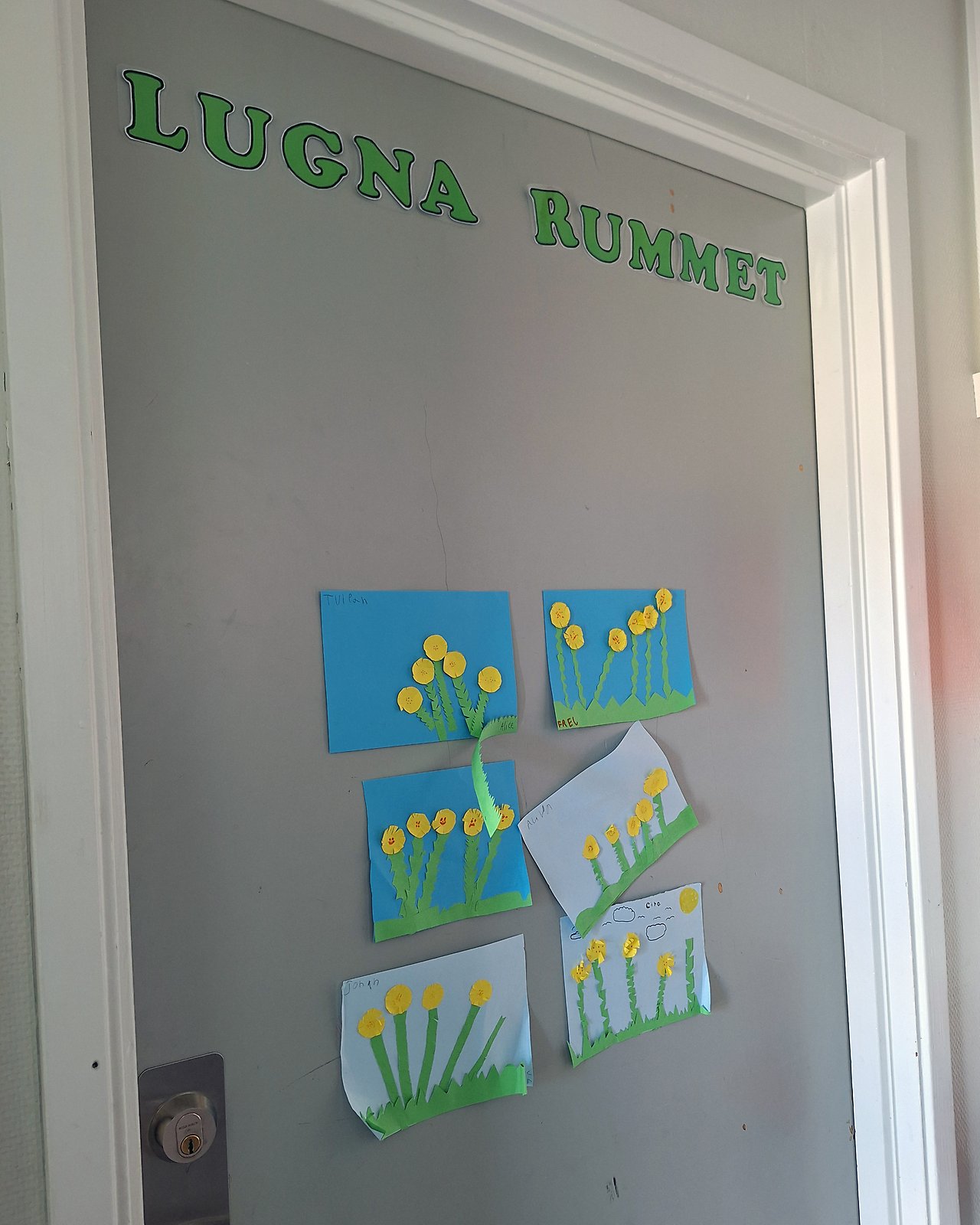 Dörr med texten ”Lugna rummet” och flera barnteckningar av blommor uppsatta på dörren.