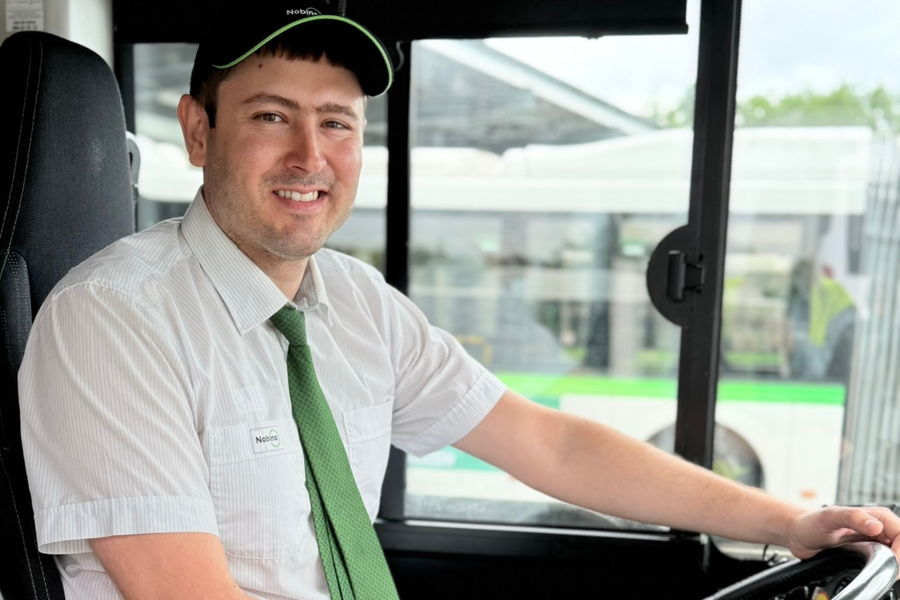 Bussförare sitter vid ratten i en buss och ler mot kameran