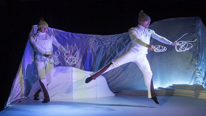 Två dansare i rörelse mot vit bakgrund. 