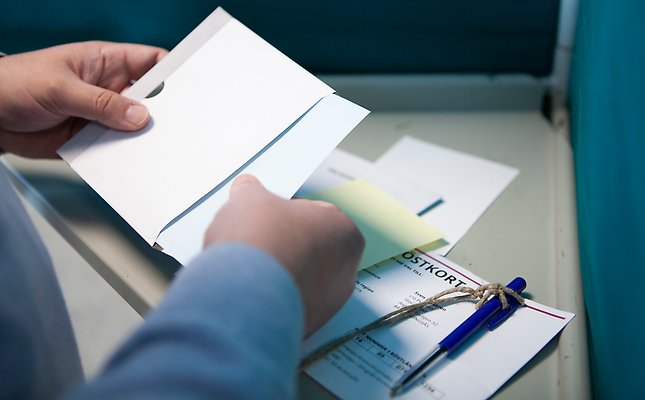 Bild som visar händer som stoppar valsedel i valkuvert.