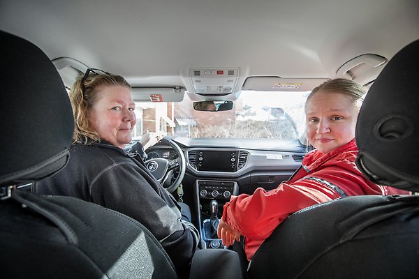 Två kvinnor sitter i framsätet i en bil och tittar bakåt på dig i baksätet. 