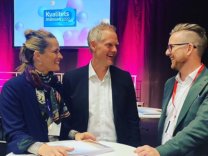 Louise Callenberg, Marcus Matteby och Mattias Robertsson Bly pratar och ser glada ut vid ett ståbord på Kvalitetsmässan 2022