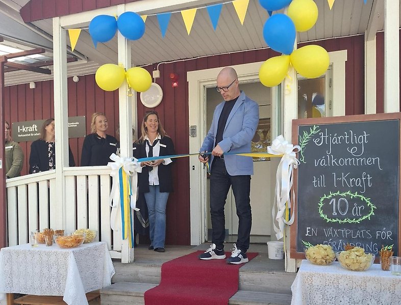 Man klipper band utanför den nya verksamheten, på fasaden hänger ballonger och blågula vimplar.
