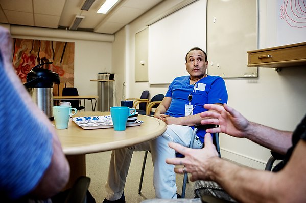 En sjuksköterska sitter vid ett bord och dricker kaffe och pratar med andra personer utanför bild.