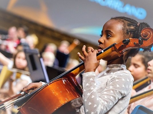 Flicka spelar på instrument, i bakgrunden syns fler barn som spelar på olika instrument.
