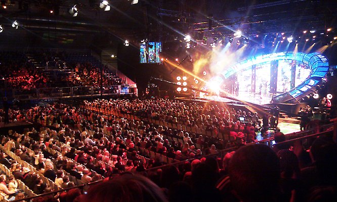 Melodifestivalen med många människor i publiken och artister på scenen.