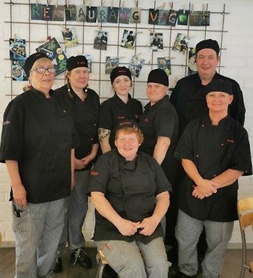 Sju personer klädda i svarta kockkläder står och sitter. I bakgrunden syns bokstäver bildandes restaurang Vagott.