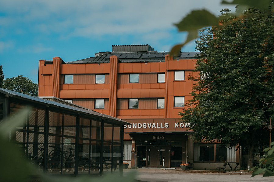 Entrén av Sundsvalls kommunhus fotat på håll genom lummig natur.